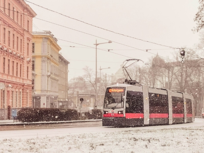 red and white tram passing historic buildings in the snow