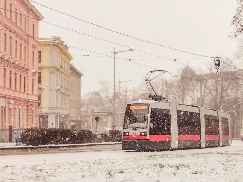 red and white tram passing historic buildings in the snow