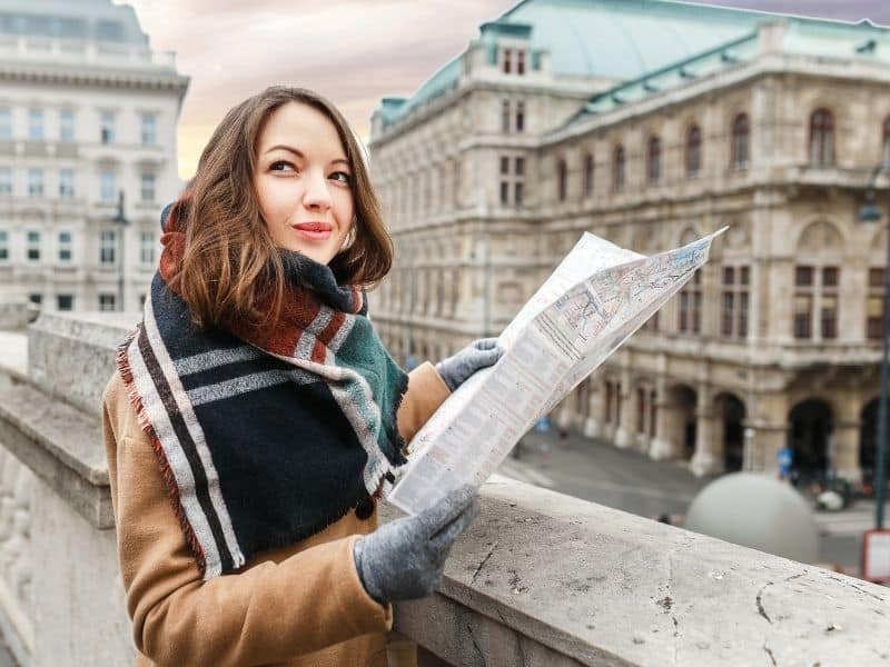 A stylish woman in a coat with a scarf is guided by a map in the center of Vienna