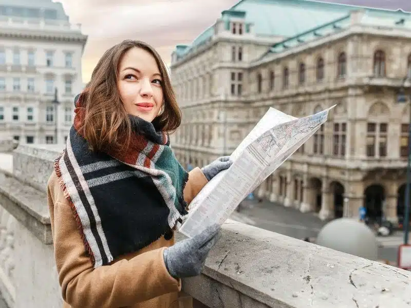 A stylish woman in a coat with a scarf is guided by a map in the center of Vienna