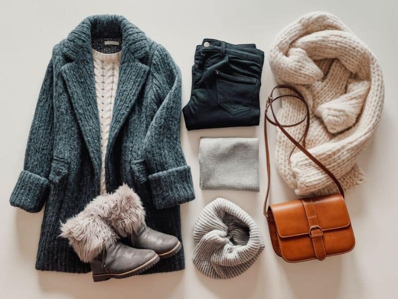 A photograph of a neatly arranged flat lay displaying a collection of women's winter clothing items ready for travel
