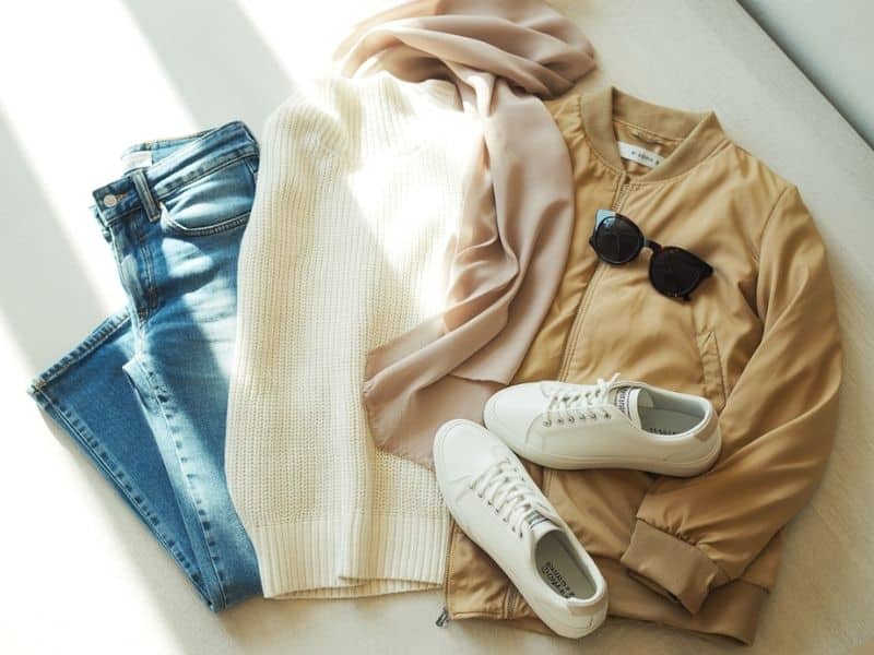 A photograph of a flat lay arrangement featuring a pair of light-wash ladies jeans neatly folded alongside a cream-colored, fine-knit lightweight jumper