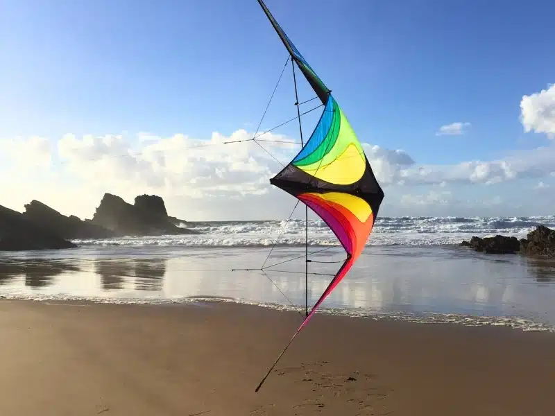Colorful stunt kite flying on a beach with a rocks and a rough sea