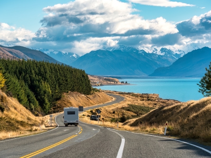 Scenic road trip of Mt Cook or Aoraki over winding road with motorhome driving and Lake Pukaki on sunny day at Peters lookout, New Zealand