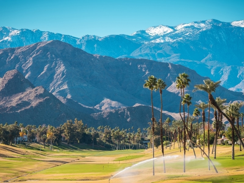 Sunny Warm Winter Time in the Palm Desert Coachella Valley. Golf Courses, Palms and Mountains Covered by Fresh Snow. Recreation in Southern California State, United States of America.
