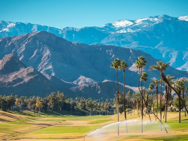 Sunny Warm Winter Time in the Palm Desert Coachella Valley. Golf Courses, Palms and Mountains Covered by Fresh Snow. Recreation in Southern California State, United States of America.