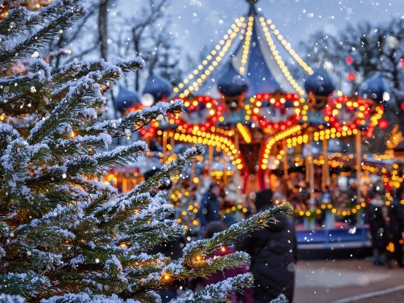 Christmas in Tivoli Gardens, Copenhagen, Denmark, with a snow covered fir tree in front of a defocussed carrousel ride
