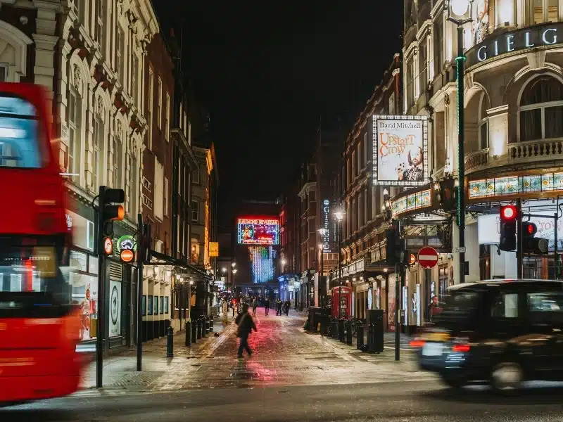 Nightime shot of a street in London's Theatre land with a red London bus and a black taxi