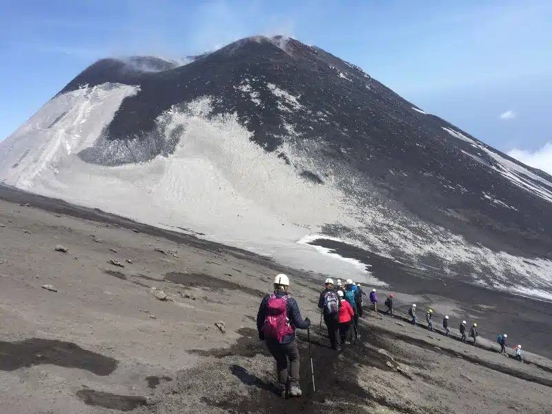 A line of hikers snakes down an ash slope on Mount Etna