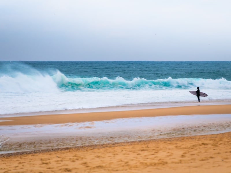 Surfer with surfboard standing on the ocean beach and waiting for the big wave. Atlantic ocean, Nazare, Portugal