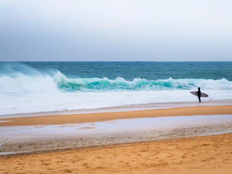 Surfer with surfboard standing on the ocean beach and waiting for the big wave. Atlantic ocean, Nazare, Portugal