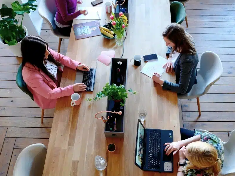 Three women working on laptops at a long wooden table