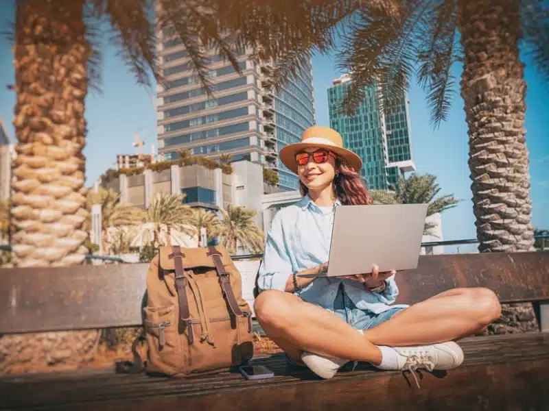 Freelancer working outdoors in Dubai using laptop, enjoying the shade of palm trees