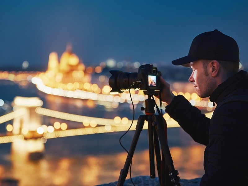 Photographer with tripod. Young man taking photo with his camera in the night city. Budapest, Hungary.