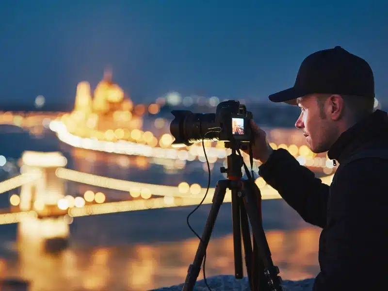 Photographer with tripod. Young man taking photo with his camera in the night city. Budapest, Hungary.