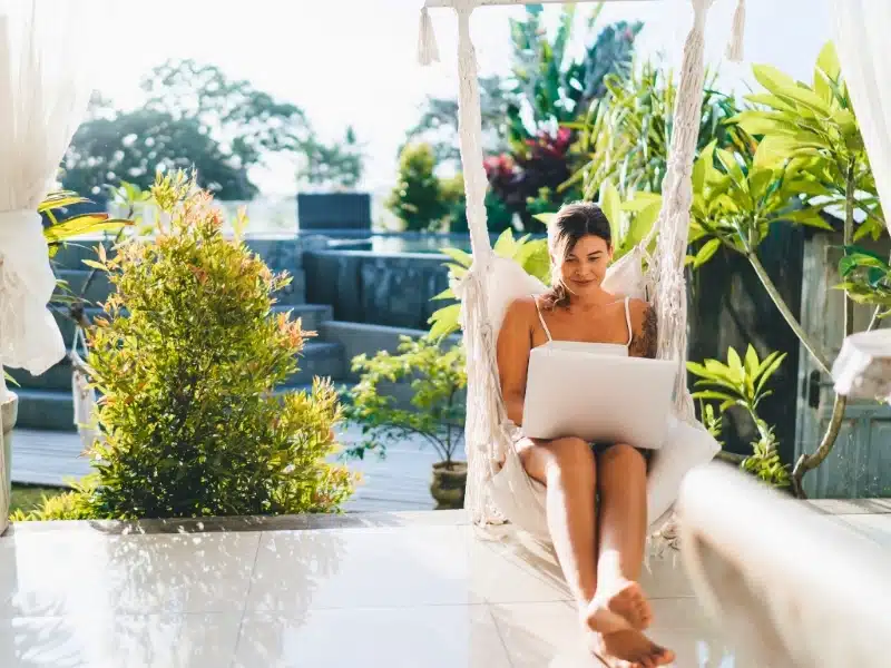 Young woman using a laptop computer on a hammock chair in Bali