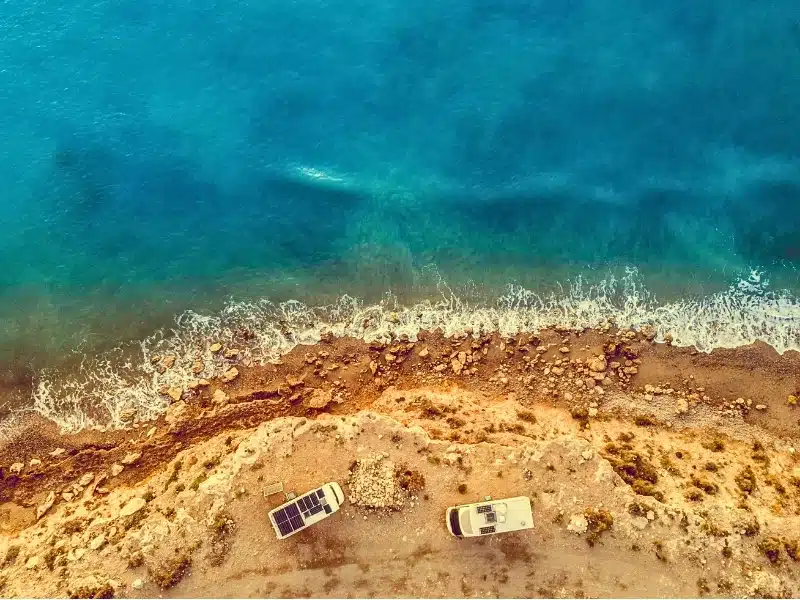 Aerial view. Two camper vehicles with solar photovoltaic panels on roof camping on sea, coastal cliff in Spain. 