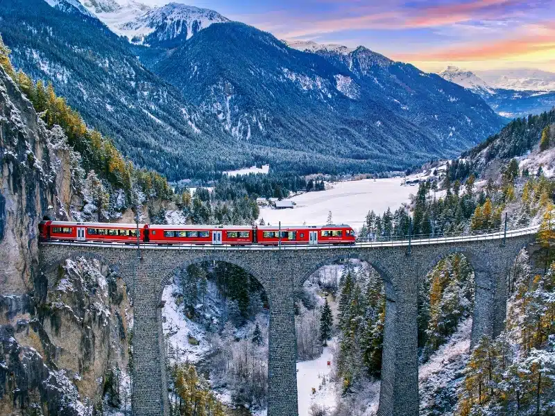 Aerial view of a train passing over the Landwasser Viaduct in the Swiss Alps.