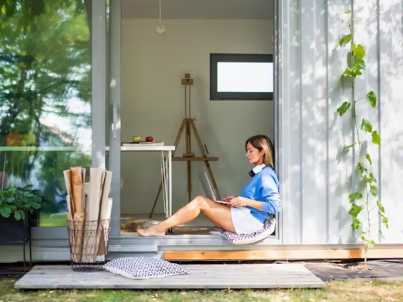 Woman working in home office in container house in backyard.