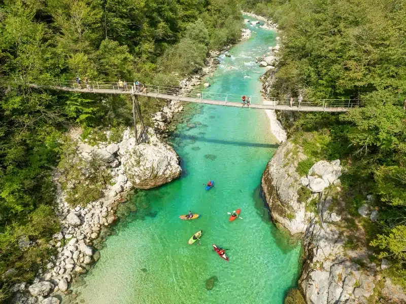 A suspension bridge spans the emerald waters of the Soca River in Slovenia. This spot is a favored destination for kayaking and trekking in Slovenia.