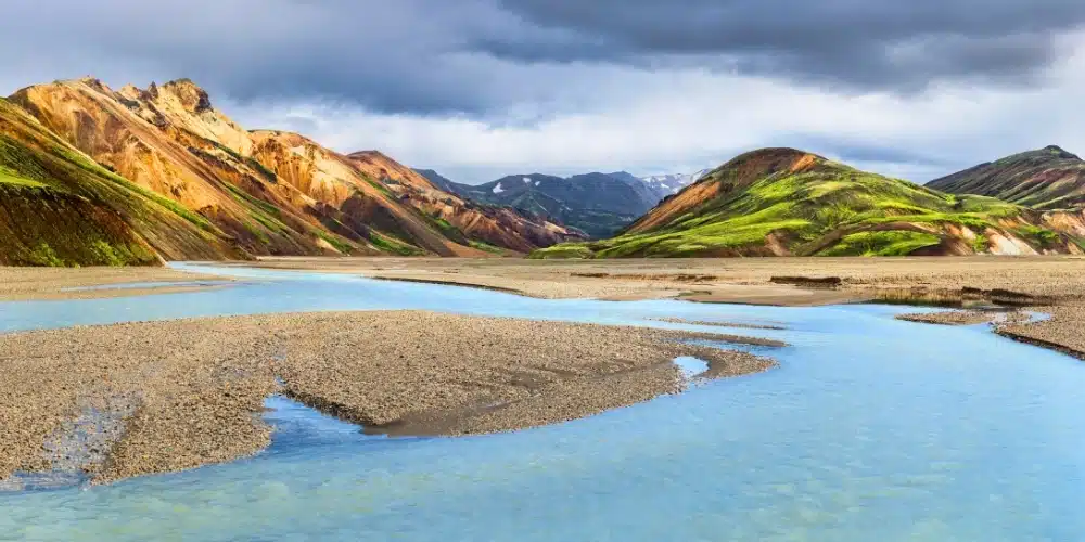 Panoramic view of Landmannalaugar in Iceland, showcasing colorful rhyolite mountains and a winding river under a dramatic sky.