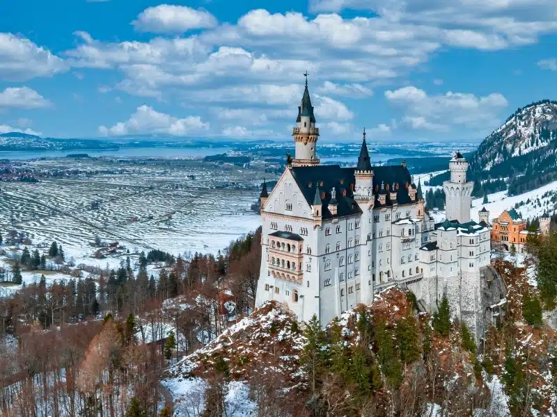 Aerial view of the Neuschwanstein Castle or Schloss Neuschwanstein  on a winter day, with the mountains and trees capped with snow all around it.