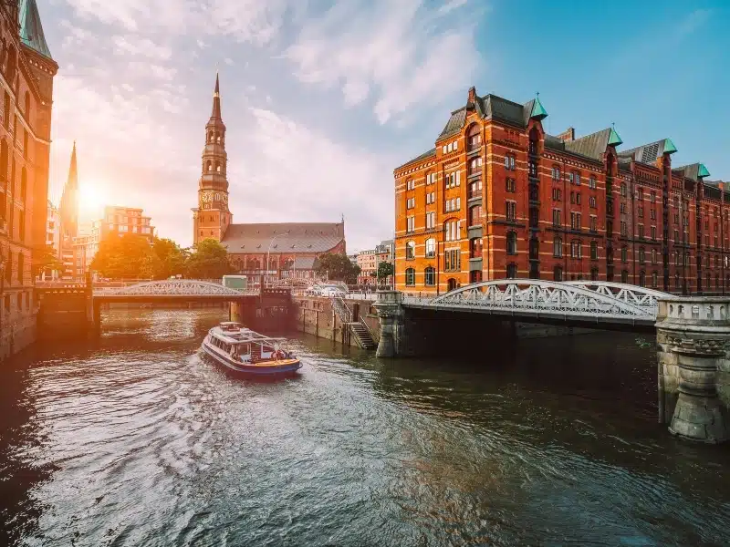 Touristic cruise boat on a channel with bridges in the old warehouse district Speicherstadt in Hamburg in golden hour sunset light, Germany