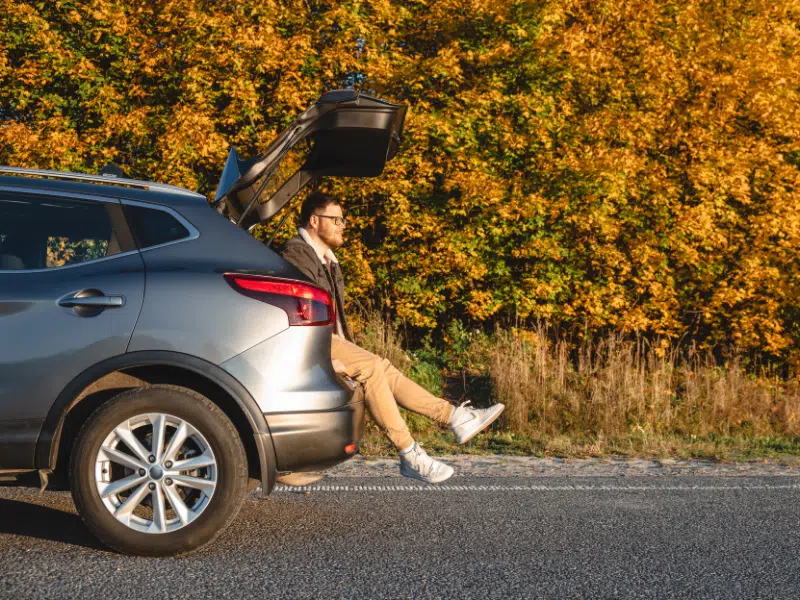 a man sits in the trunk of a car and enjoys the autumn sun