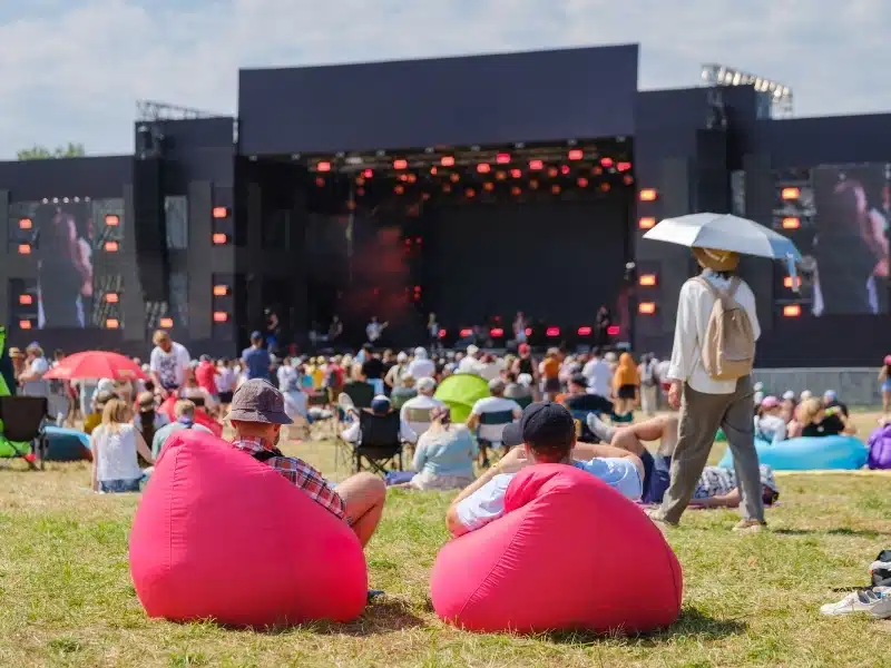 Summer festival vibes with enthusiastic crowd relaxing and watching a live concert outdoors under clear skies.