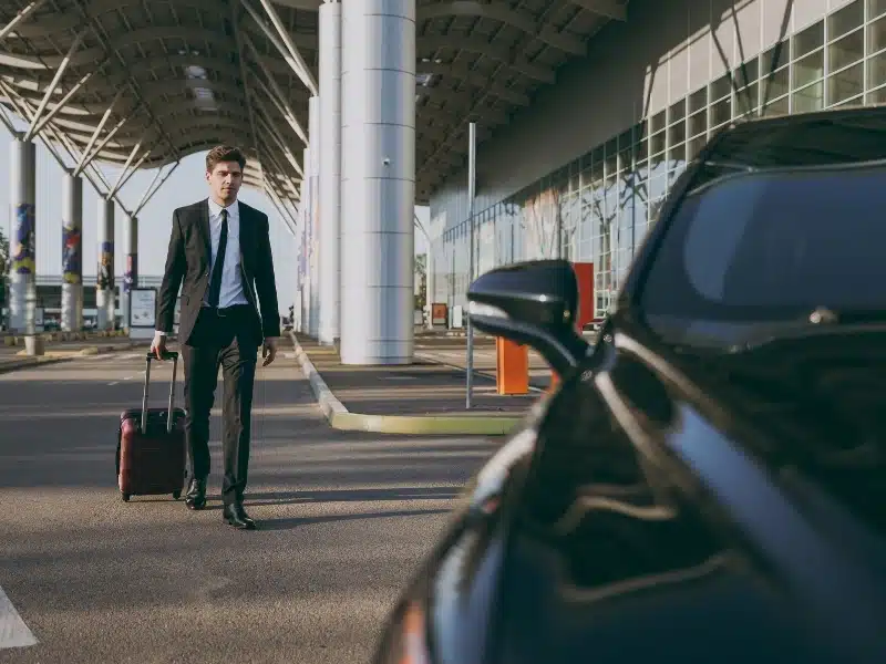 Businessman at international airport terminal walking with suitcase to car.