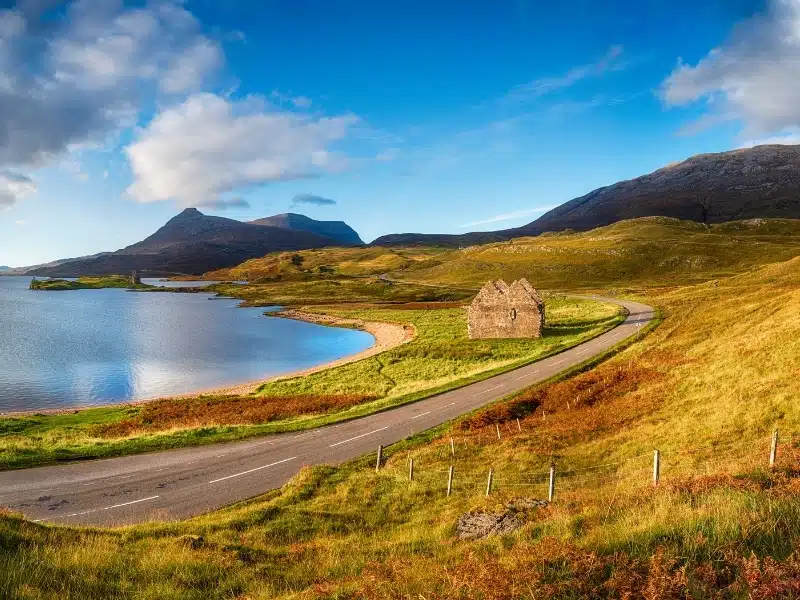 Autumn at Loch Assynt in Scotland with the ruins of Calda House and Ardvreck Castle in the far left, landmarks on the NC500 scenic driving route