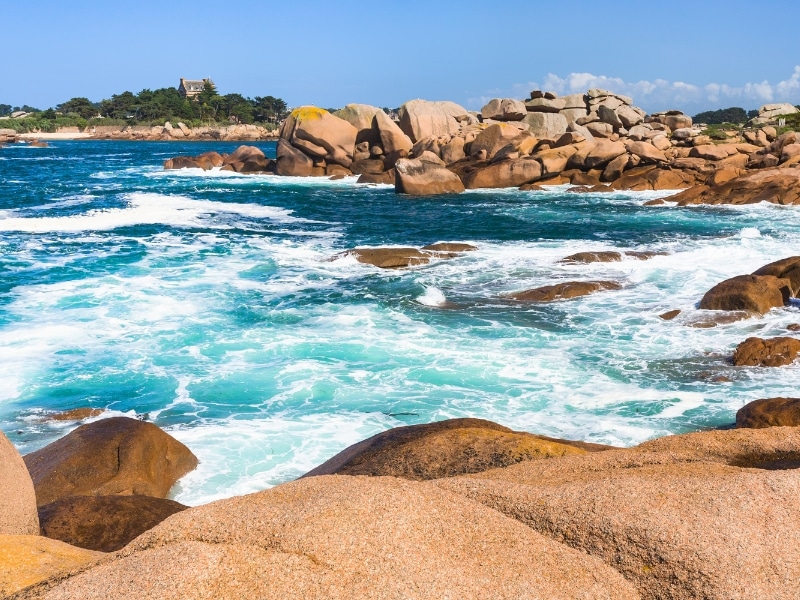Rocky pink coastline with turquoise sea splashing on the boulders