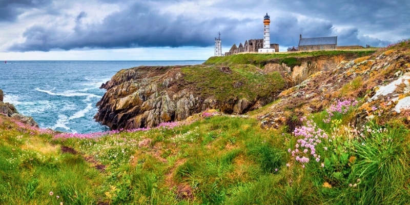 Panorama of a lighthouse and ruins atop a cliff with sea views and stormy skies