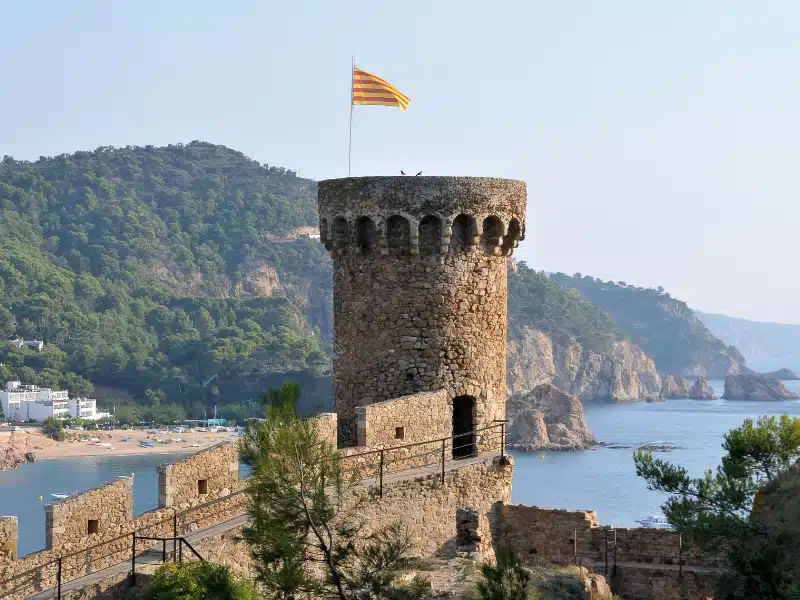 Detail of one round stone tower of a walled city above the sea, flying a yellow and red striped flag