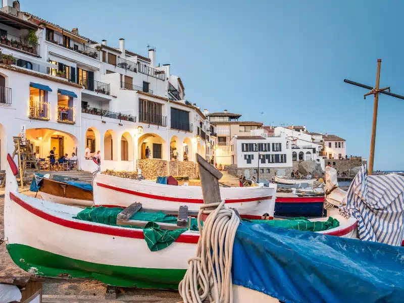red white and green boats pulled up on a sandy shore in front of low-rise white buildings