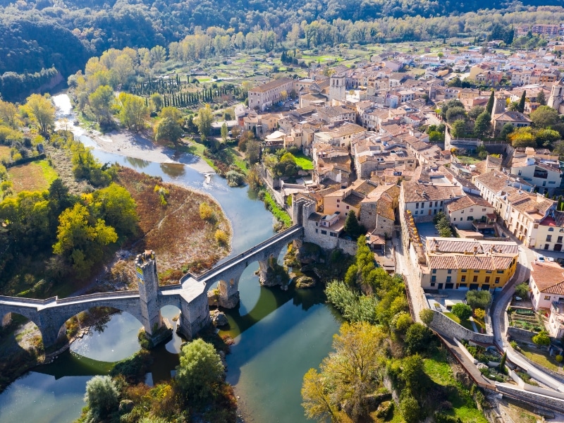 Aerial shot of a red roofed Medieval town by a river and arched bridge