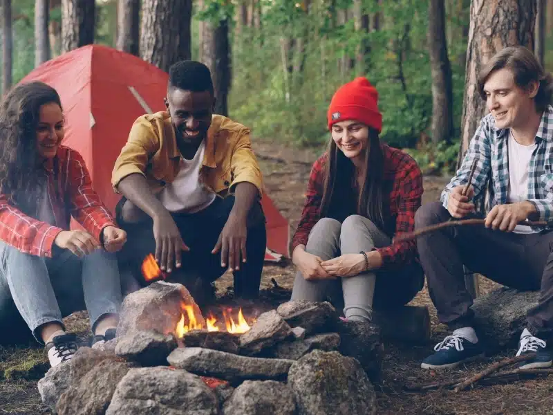 Group of friends around a campfire with a red tent in the background