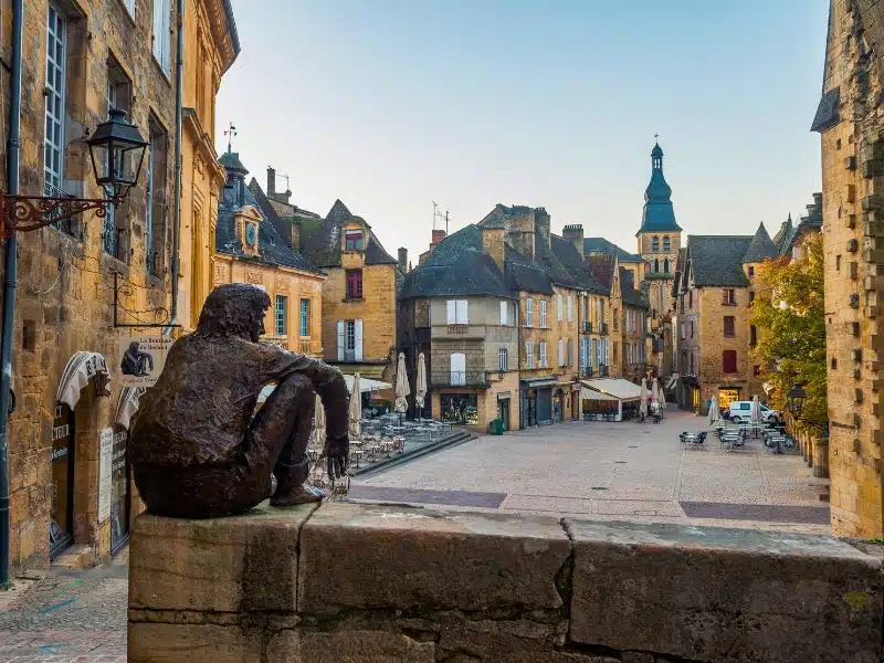 Bronze sitting statue overlooking. atypical French square awaiting evening diners