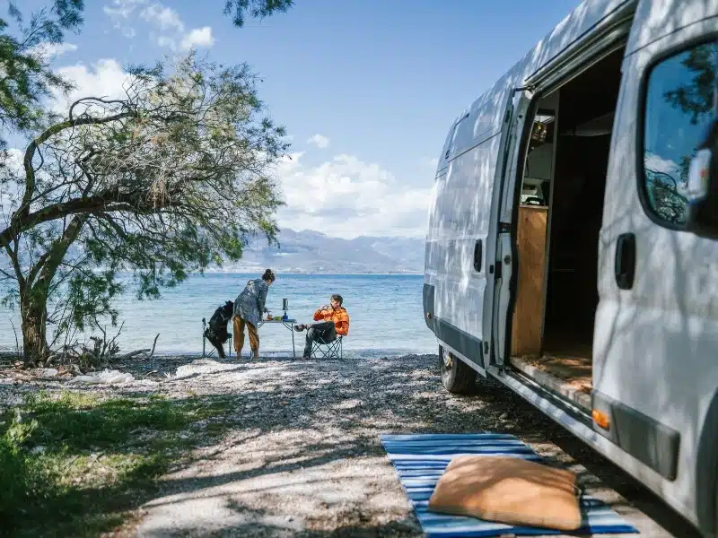 Couple at a camping table by a white van and the sea