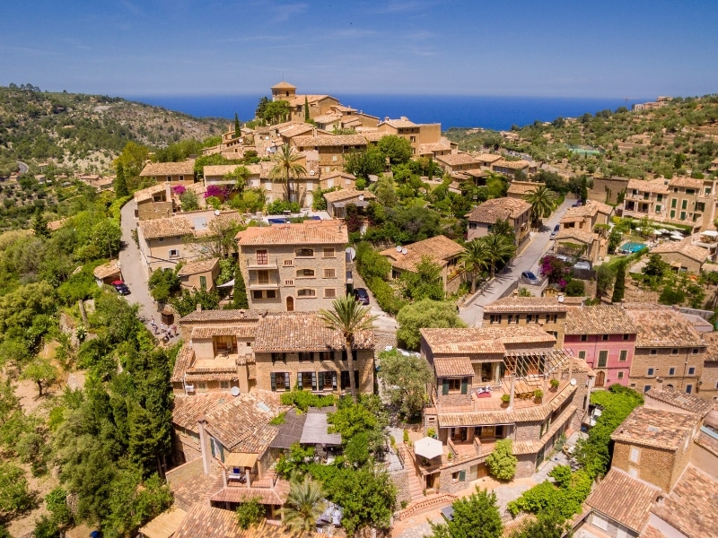 Aerial view to the sea over a small stone village with terracotta roofs and palm trees