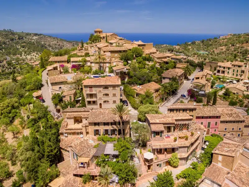 Aerial view to the sea over a small stone village with terracotta roofs and palm trees