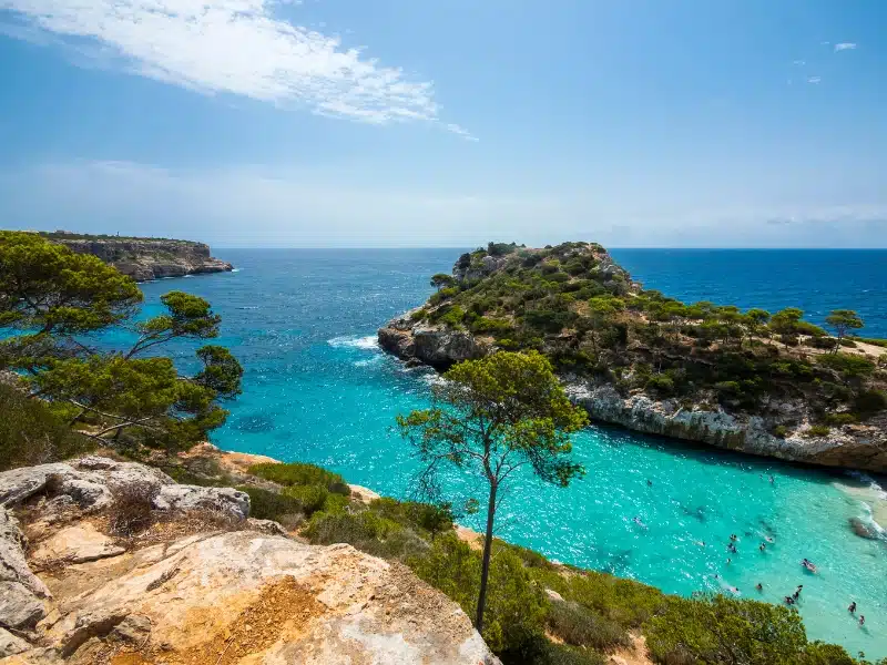 Turquoise water over fine sand surrounded by rocky outcrops and trees
