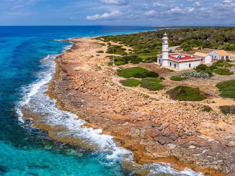 Red and white lighthouse on a rocky wooded shoreline