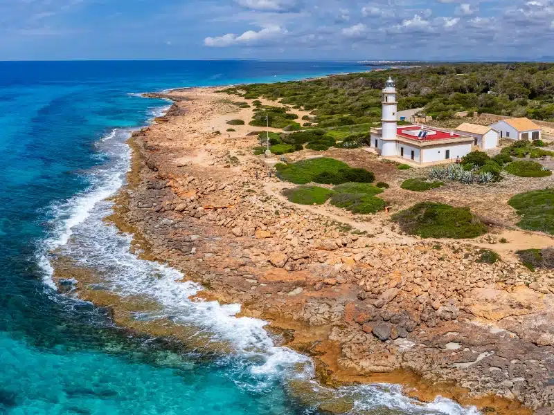 Red and white lighthouse on a rocky wooded shoreline