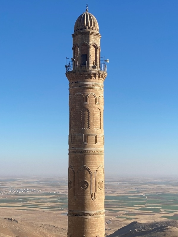 ornate brick minaret against a blue sky and vast plains