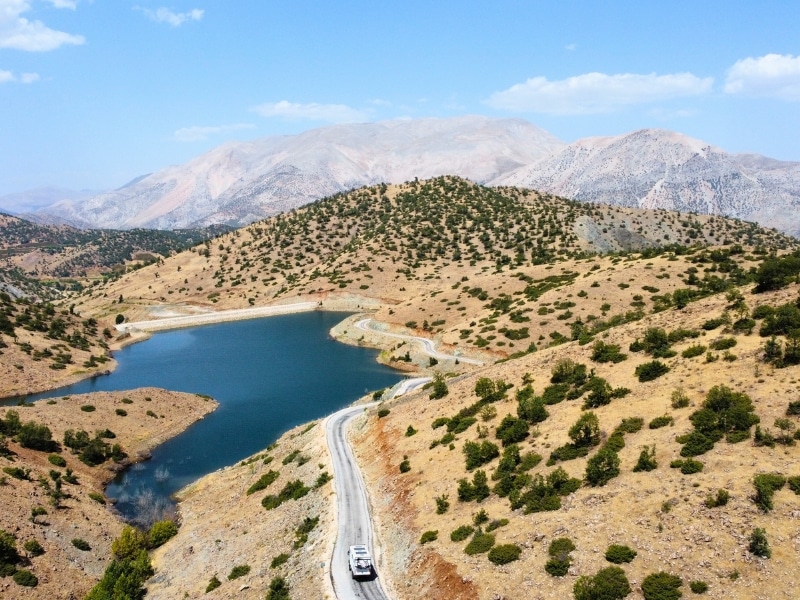 Road around a reservoir surrounded by mountains and hills covered in shrubs