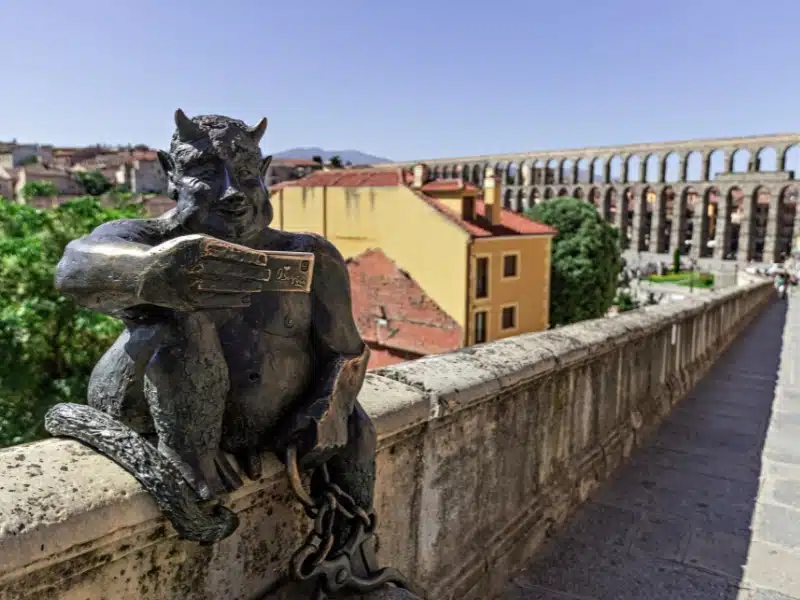 View of the Estatua del Diablo, a bronze statue of a smiling devil taking a selfie photo of itself sited in the city of Segovia Spain