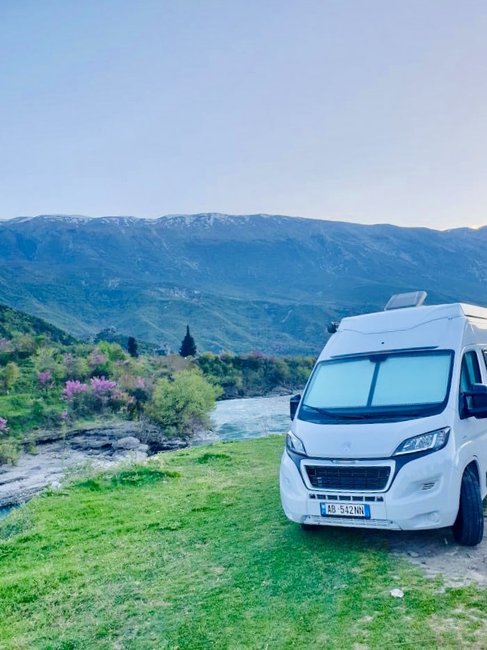 Motorhome parked on a grassy verge by a river with a mountain backdrop
