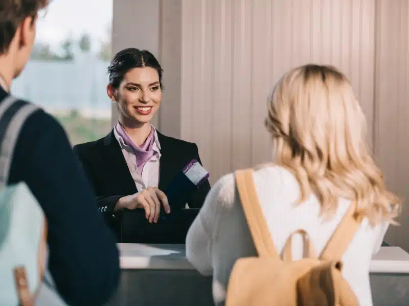 back view of young couple looking at smiling airport worker at check-in desk
