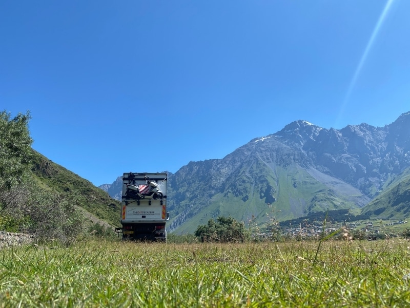 white overland truck parked ona. grassy meadow with a mountain backdrop